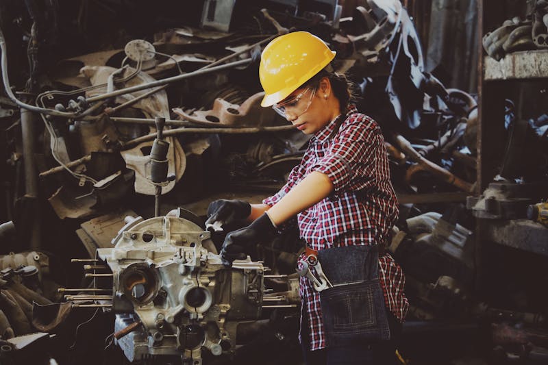Woman in hard hat and safety gear working on vehicle parts