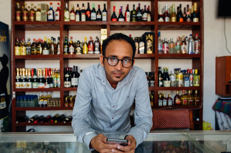 Liquor store owner behind counter with shelves of wine and spirits